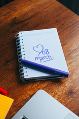 Photograph of notebook on a wooden table with hand drawn March 8 heart. Concept of people and lifestyles.
