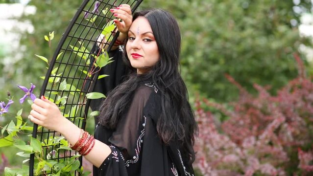 Brunette woman in black dress standing near lattice arch in park