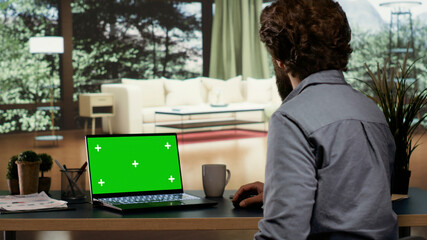 Entrepreneur uses pc with greenscreen display at his luxurious vacation home, feeling cozy in his expensive villa in the forest. Rich CEO investor looking at blank mockup template on laptop. - obrazy, fototapety, plakaty