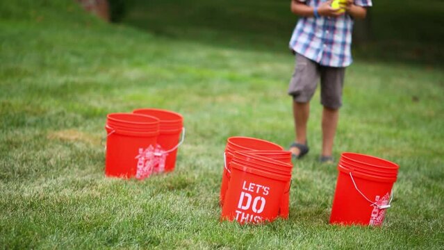 Boy stands next to red buckets and balls fall into bucket