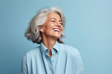 Portrait of happy senior woman laughing and looking at camera on blue background