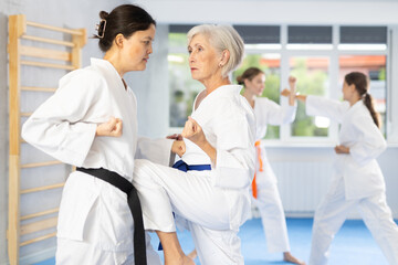 Fototapeta premium Mature woman in pair exercising karate movements during group training