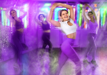 Smiling young girl performing energetic dynamic dance during group training in studio. Colorful toned image with motion blur and vivid light effects