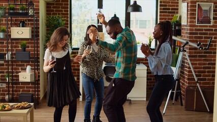 Multiracial school colleagues organizing apartment party, enthusiastically dancing to electronic...