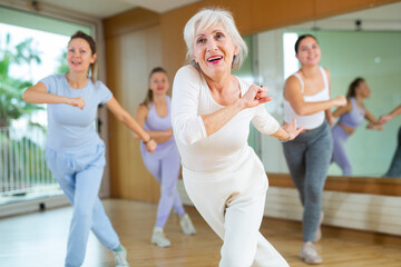 Active aged woman practicing aerobic dance in training hall during fitness dance classes. Women...