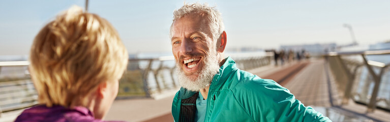 After morning run. Cheerful mature bearded man in sportswear talking with his wife and smiling...