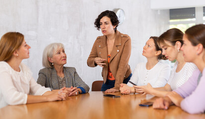 Positive motivated young Hispanic woman team leader holding meeting with group of fellow female students of different ages sitting around desk, explaining details of new study project