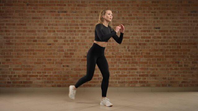 Alternative reverse lunges. A trainer skillfully demonstrates how to perform the exercise, alternative reverse lunges. A girl in good physical shape. She is in black sportswear in a loft gym. 8K RAW.