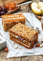 Two slices of delicious honey biscuit cake with cream, apples, cherries and peanuts on wooden background with cup of tea and spring flowers. Sweets, dessert and pastry, homemade cakes, close up