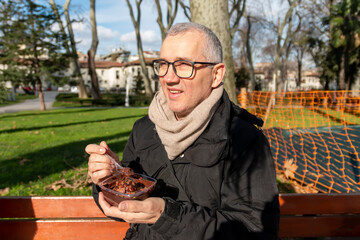 Mature man sitting on bench in park  and enjoying a sweet and delicious cake. Street foods are popular among tourists and people. Food concept.