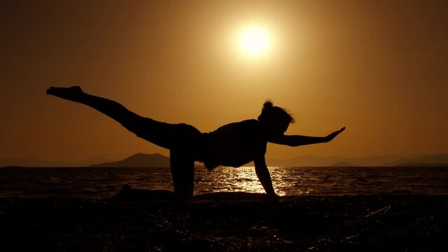 Woman silhouette stretching back on shore. An active woman silhouette stretching on the beach and enjoy asana against orange sunset in summer.