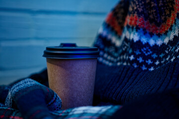 Winter clothes and gloves lie next to a cup of coffee, against the background of a cold brick wall,...