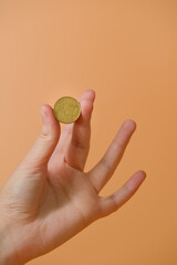 A women's hand holding a 50 euro cent coin, on an orange background, close-up