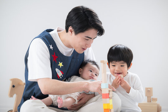 Image of male childcare worker changing careers Smiling childcare worker and toddler playing with building blocks indoors
