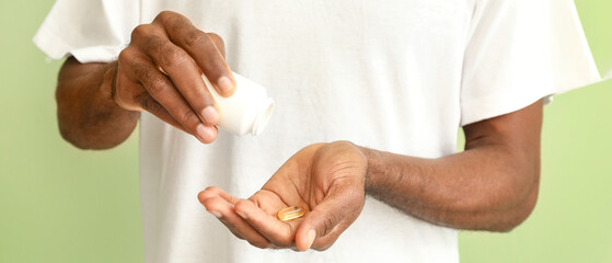 African-American man with fish oil on green background, closeup