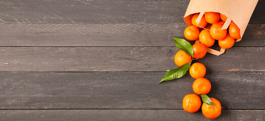 Paper bag and tasty scattered tangerines on wooden background with space for text