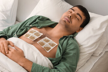 Ill young man with mustard plasters on his chest sleeping in bedroom