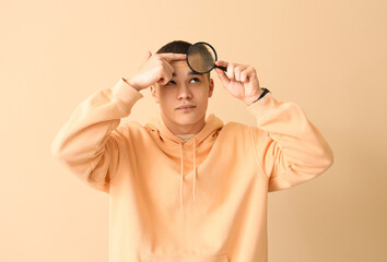 Teenage boy with acne and magnifier on beige background