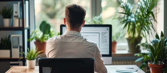Businessman at office desk completing survey form on computer, seen from behind.