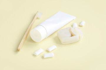 Toothpaste with brush, dental floss and chewing gums on light yellow background