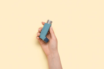 Female hand with asthma inhaler on yellow background