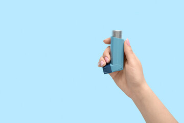 Female hand with asthma inhaler on blue background