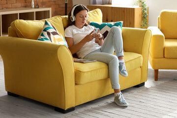 Young woman in headphones using mobile phone on her day off at home