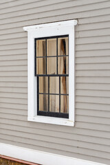 The exterior wall of a grey coloured building is made of narrow horizontal wooden clapboard.  There's a single hung closed block glass window with white crown trim molding and black glass dividers.