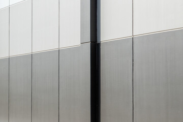 The exterior wall of a contemporary commercial style building with two shades of grey aluminum metal composite panels. The futuristic building has engineered diagonal cladding steel frame panels. 