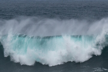 An angry turquoise green colour massive rip curl of a wave as it rolls along a beach. The white...