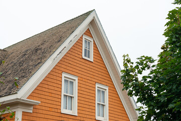 The top floor of an orange colored frame house or cottage with multiple small double hung windows. The trim on the wooden house is cream in color. The sky is cloudy and there's a tall green tree. 