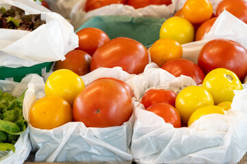 A display of various fresh tomatoes harvested for sale at a grocery. The produce is vibrant yellow, red and orange color with a firm and shiny skin.The tomatoes are stored in square white plastic bins