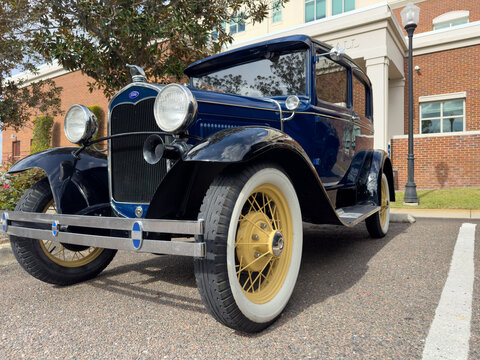 Orlando, Florida, US: A navy blue classic two-door car, a Ford Model T. The front of the automobile has a long chrome grate with large round headlights. The front cab has a flat glass window. 