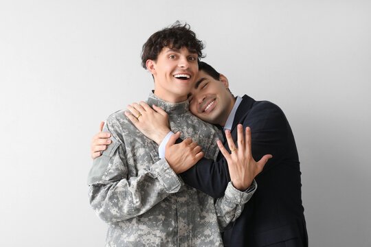 Young soldier with his husband hugging on light background
