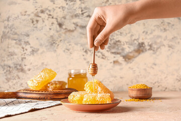 Woman pouring sweet honey onto combs on beige background