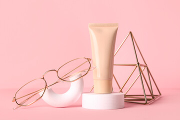 Composition with liquid foundation, eyeglasses and decorative pyramid on pink background