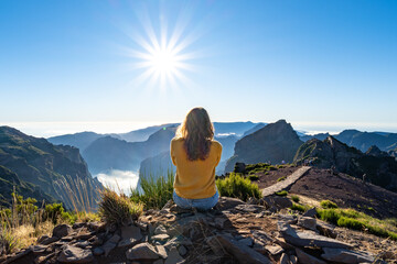 A female tourist sits on the top of a mountain and enjoys the panoramic view over a volcanic island on a sunny summer afternoon. Pico do Arieiro, Madeira Island, Portugal, Europe.