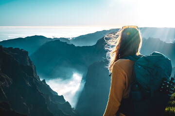 Female backpacker tourist looking at a deep, cloud-covered valley and enjoying the breathtaking view of the volcanic mountain landscape. Pico do Arieiro, Madeira Island, Portugal, Europe. - obrazy, fototapety, plakaty