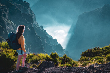 Tourist stands on the edge of a deep, cloud-covered valley and enjoys the breathtaking view into...