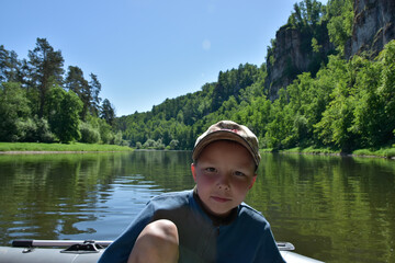 A boy in a cap floats on a rubber boat on the river.