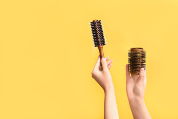 Female hands with comb rollers on yellow background.