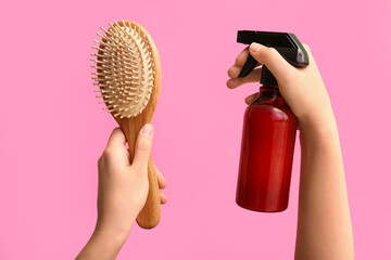 Female hands with hairbrush and sprayer on pink background.