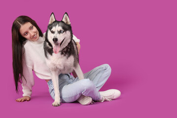 Beautiful young woman with Husky dog on purple background