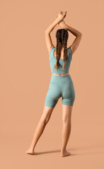 Sporty young woman in cycling shorts on beige background, back view