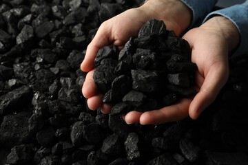 Man holding coal in hands over pile, closeup. Space for text