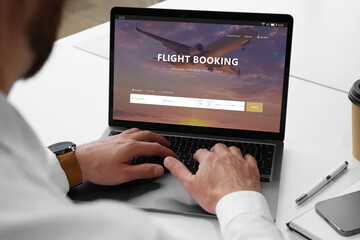 Man using laptop to book flight at white table, closeup