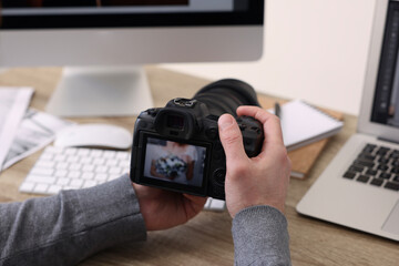 Professional photographer with digital camera at wooden table indoors, closeup