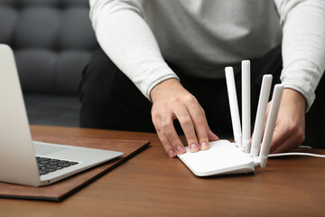Man inserting cable into Wi-Fi router at wooden table indoors, closeup