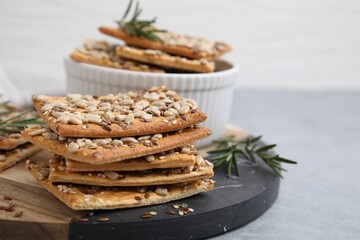 Cereal crackers with flax, sunflower, sesame seeds and rosemary on grey table, closeup