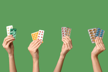 Female hands holding pills in blister packs on green background - obrazy, fototapety, plakaty